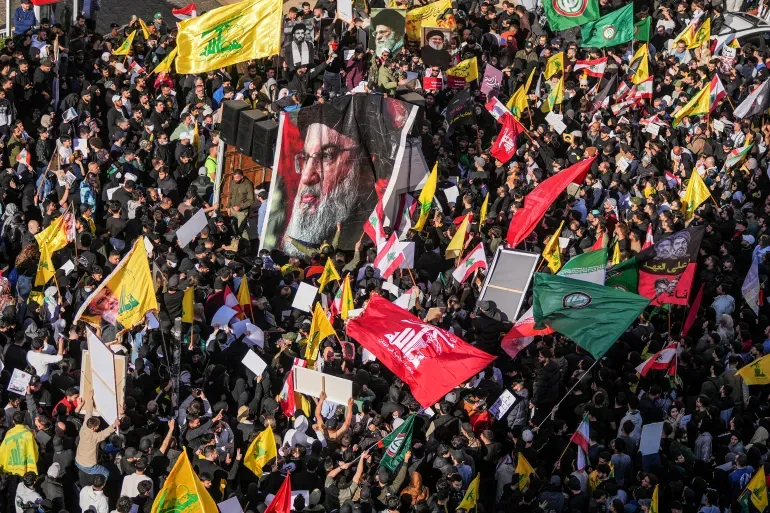 Người biểu tình vẫy cờ Lebanon và Hezbollah, đồng thời cầm ảnh chân dung các lãnh đạo Hezbollah khi họ tập trung biểu tình phản đối Thủ tướng Lebanon Nawaf Salam bên ngoài cung điện chính phủ ở Beirut, Lebanon [Ảnh của Hassan Ammar/AP].